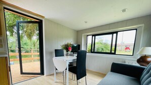 A modern living room with a sofa, a dining table with chairs, a TV, and a window with a view of greenery. - A little corner of paradise (Église-Neuve-de-Vergt)