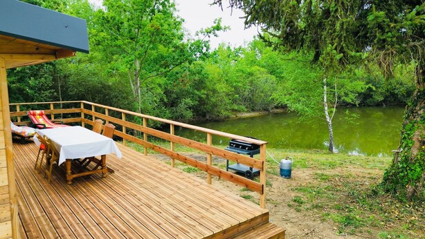 A wooden deck with a table and chairs, overlooking a river surrounded by trees. - A little corner of paradise (Église-Neuve-de-Vergt)