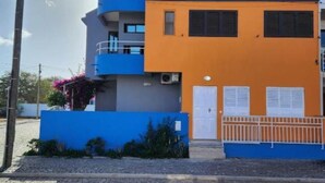 Ein zweistöckiges Gebäude mit einer blauen und orangen Fassade, einer weißen Tür und einem kleinen Balkon.