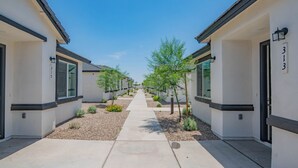 A pathway leading to a row of modern buildings with numbered doors, surrounded by small trees and gravel. - The One 313 (Glendale)