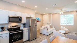 A modern kitchen with stainless steel appliances, a dining area with a wooden table and chairs, and a living area with a sofa and a ceiling fan. - The One 313 (Glendale)