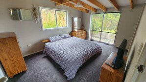 Une chambre à coucher avec un grand lit, une commode, une coiffeuse et un téléviseur posé sur un meuble en bois.
