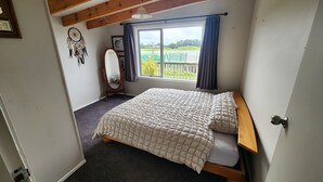 Une chambre à coucher avec un lit, une fenêtre avec des rideaux, un attrape-rêves et un tableau encadré au mur.