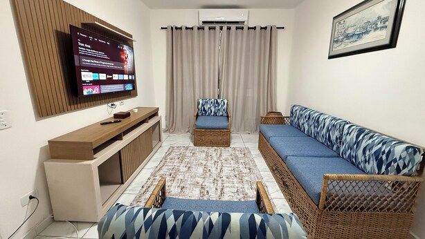 A living room with a flat-screen TV, a sofa, a chair, and a small table.