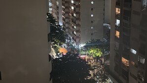 A nighttime view of a residential area with high-rise buildings, illuminated windows, and a street with parked cars and trees.