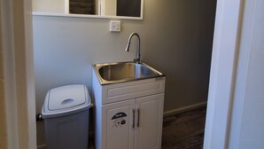 Een kleine kitchenette met een spoelbak, een prullenbak en een spiegel met verlichting erboven.