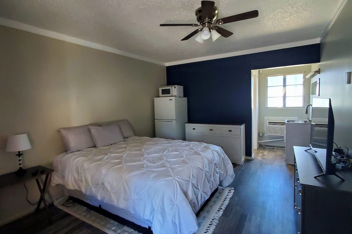A bedroom with a bed, a ceiling fan, a dresser, a desk, and a window.
