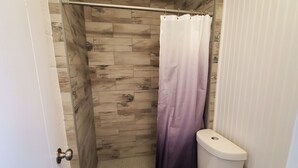 Een badkamer met een douche, toilet en houten vloer.