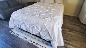 Een slaapkamer met een groot bed, een grijze bank, een nachtkastje met een lamp en een kleine tafel.
