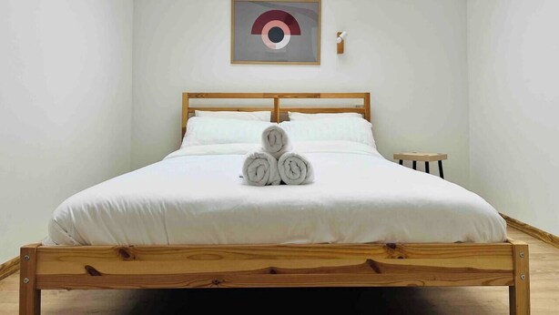 A neatly made bed with rolled towels in the center, a wooden headboard, and a skylight above. - Spacious 3BR Apt • 110sqm • Carol Park • Balcony (București)