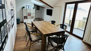 A dining area with a wooden table and chairs, a white wall with framed pictures, and a large window with a view of the outside. - Spacious 3BR Apt • 110sqm • Carol Park • Balcony (București)