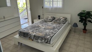 Una camera da letto con un letto, una cassettiera, un comodino, una pianta in vaso e una finestra con vista sull'esterno.
