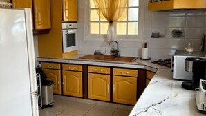 Una cucina con mobili gialli, un frigorifero bianco, una finestra con tende gialle, un lavello e un piano di lavoro con una macchina per il caffè.