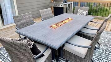 A rectangular outdoor table with a built-in fire feature, surrounded by wicker chairs with cushions.