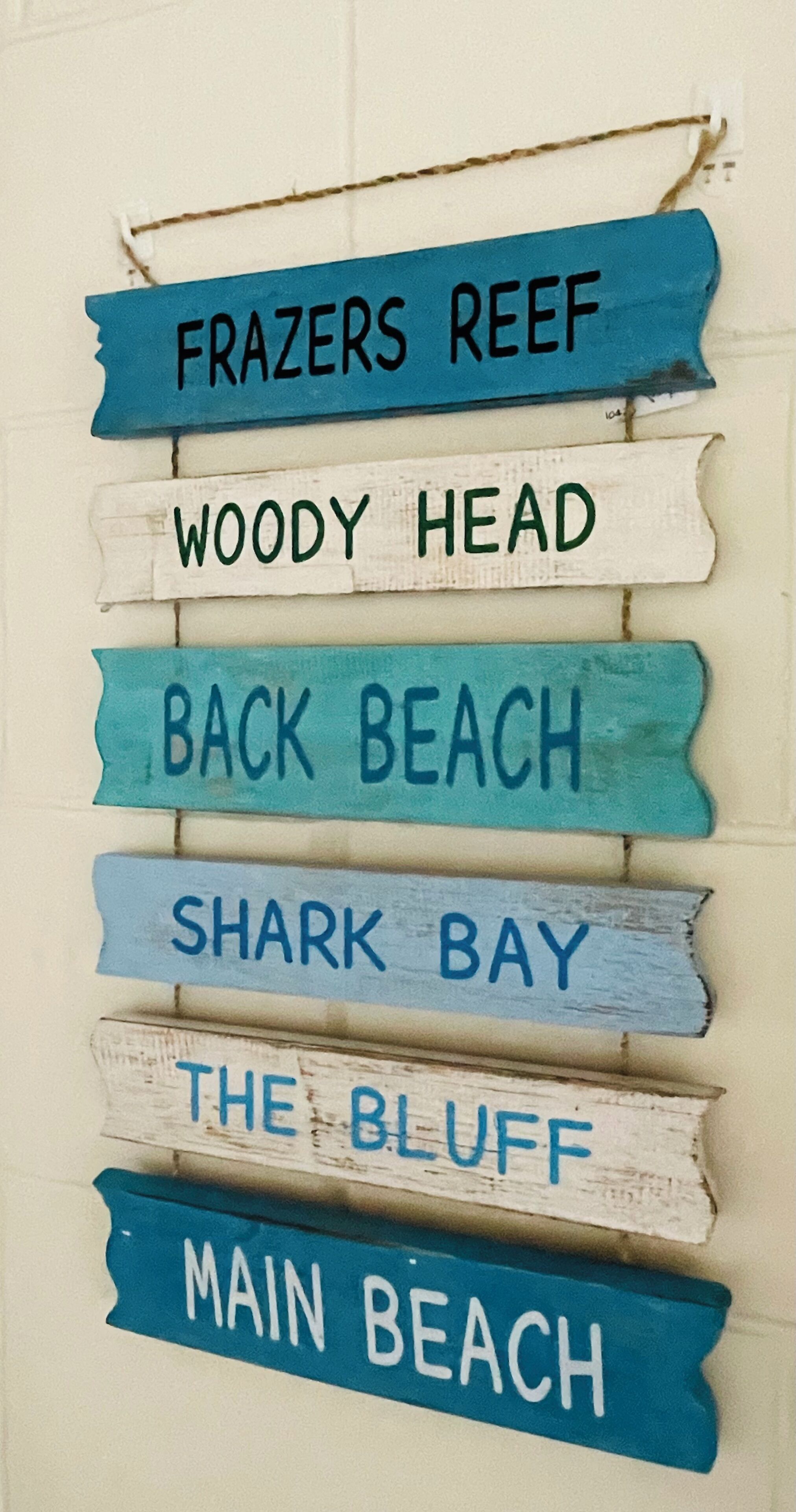 A wall with painted wooden signs indicating beach names.