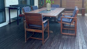 An outdoor patio with a wooden table and chairs, a small plant, and a metal grill.