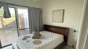 A bedroom with a large bed, a wooden headboard, a white brick wall, and a view of a wooden deck outside.
