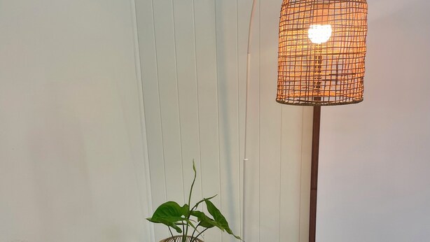 A floor lamp with a woven shade, a small round table with a plant, and a wall socket.