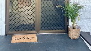 A double door with a mesh screen, a welcome mat, and a potted plant.