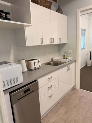 A modern kitchen with white cabinets, a built-in dishwasher, and a toaster. - Superb 3-bedroom house with AC in charming Iluka (Iluka)