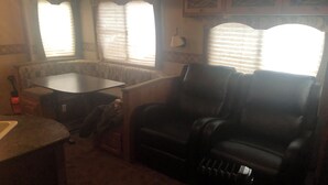 A small, dimly lit room with a single black leather chair, a small table, and a radiator. - Cozy 1-bedroom camper sleeps up to 4 
Daily/ weekly / monthly rate’s available (Kingfisher)