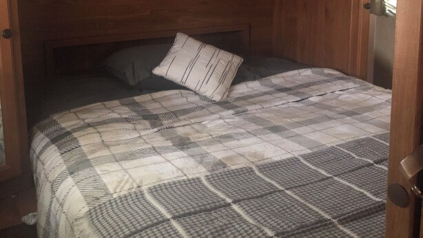 A compact bedroom with a bed, a pillow, and wooden cabinets above. - Cozy 1-bedroom camper sleeps up to 4 
Daily/ weekly / monthly rate’s available (Kingfisher)