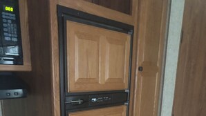 A compact kitchen with wooden cabinetry, a built-in microwave, and a stove. - Cozy 1-bedroom camper sleeps up to 4 
Daily/ weekly / monthly rate’s available (Kingfisher)