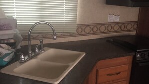 A kitchen with a sink, wooden cabinets, a countertop, and a window with blinds. - Cozy 1-bedroom camper sleeps up to 4 
Daily/ weekly / monthly rate’s available (Kingfisher)