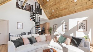 Un vaste espace de vie comprenant un grand canapé d’angle blanc, un plafond en bois et un escalier en colimaçon.