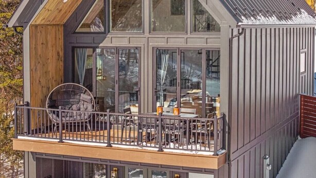 Une maison moderne dotée d’un balcon, de grandes fenêtres et d’une terrasse en bois.