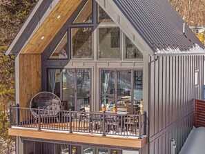 Ein modernes Haus mit Balkon, großen Fenstern und einer Holzterrasse.