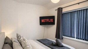 A modern bedroom with a bed, pillows, a bedside table, a lamp, a TV mounted on the wall, and a window with curtains. - Long Contractor Stays - HS2 NEC BHX Parking Wifi Netflix Discounts Offered (Birmingham)