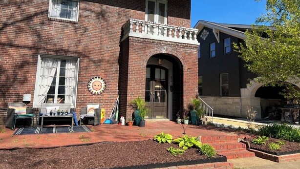 A brick building with a porch, a sun clock, and potted plants.