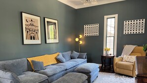 A living room with a sectional sofa, a small table with a vase, and a chair with a throw blanket.