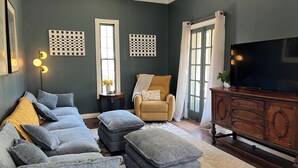 A living room with a sofa set, ottomans, a television, and a wooden cabinet.