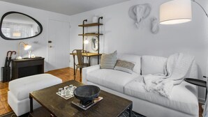 Una sala de estar moderna con un sofá blanco, una mesa de centro de madera, una mesa de comedor con sillas, una chimenea y un espejo grande en la pared.