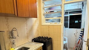 Een kleine keuken met houten kastjes, een gasfornuis, een spoelbak en een raam met zonwering.