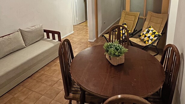 Een eethoek met een ronde houten tafel, vier stoelen, een plafondventilator en uitzicht door een glazen deur.