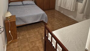 Een kleine, goed verlichte slaapkamer met een enkel bed, een houten garderobe, een plafondventilator en een raam met gordijnen.