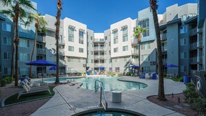 A hotel pool area with multiple lounge chairs and umbrellas, surrounded by palm trees and modern buildings. - Access 3011 (Tempe)