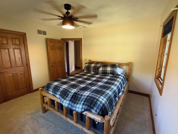 A bedroom with a wooden bed frame, a plaid bedspread, and a ceiling fan. - Secluded 4-bedroom home. 15 min to TBK sports complex & TPC Deere Run golf. (Geneseo)