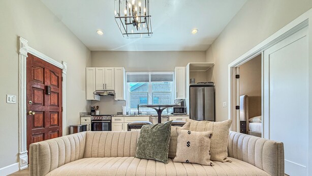 A cozy living room with a beige sofa, a wooden coffee table, and a kitchen in the background.