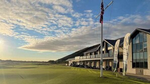 Ein Golfplatz mit Clubhaus, das einen modernen Stil, große Fenster und einen Fahnenmast mit einer amerikanischen Flagge aufweist.
