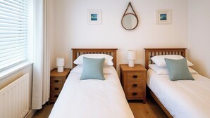 Ein Hotelzimmer mit zwei Einzelbetten, Holz-Nachttischen, Nachttischlampen und Meerblick durch die Jalousien.