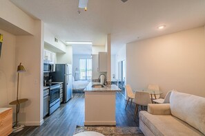 A modern kitchen with a central island, a dining area with a glass table, and a living room with a sofa. - Access 3104 (Tempe)