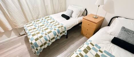 A bedroom with two beds, a wooden nightstand, a lamp, and a window with curtains.