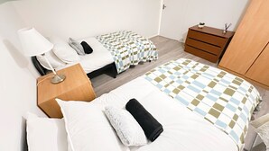 Ein Schlafzimmer mit zwei Betten, einem Nachttisch, einer Kommode, einer Lampe und einem kleinen Tisch mit einer Pflanze.
