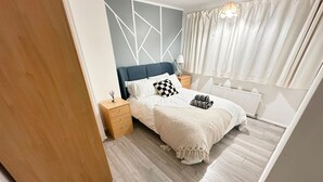 Ein modernes Schlafzimmer mit Bett, Nachttisch, Kommode und einem Fenster mit Vorhängen.