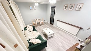 Ein Wohnzimmer mit einem grünen Sofa, einem weißen Couchtisch und einem Essbereich mit Stühlen und einem Tisch.