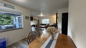 A dining area with a wooden table, chairs, and a vase of dried flowers. There is a window with a view of trees and a sign above it. - Olympic Peninsula Vacation Rental: Close to Water (Sekiu)